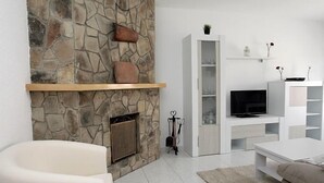 Una sala de estar moderna con chimenea de piedra, mobiliario blanco y televisor.