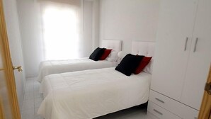 Habitación de hotel con dos camas, paredes blancas y un armario.