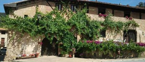 A stone building with a tiled roof, arched entrance, and lush greenery.