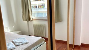 A bedroom with a bed, a radiator, a window with curtains, and a wooden floor. - HOLIDAY APARTMENT IN THE HEART OF VALPOLICELLA (San Pietro In Cariano)