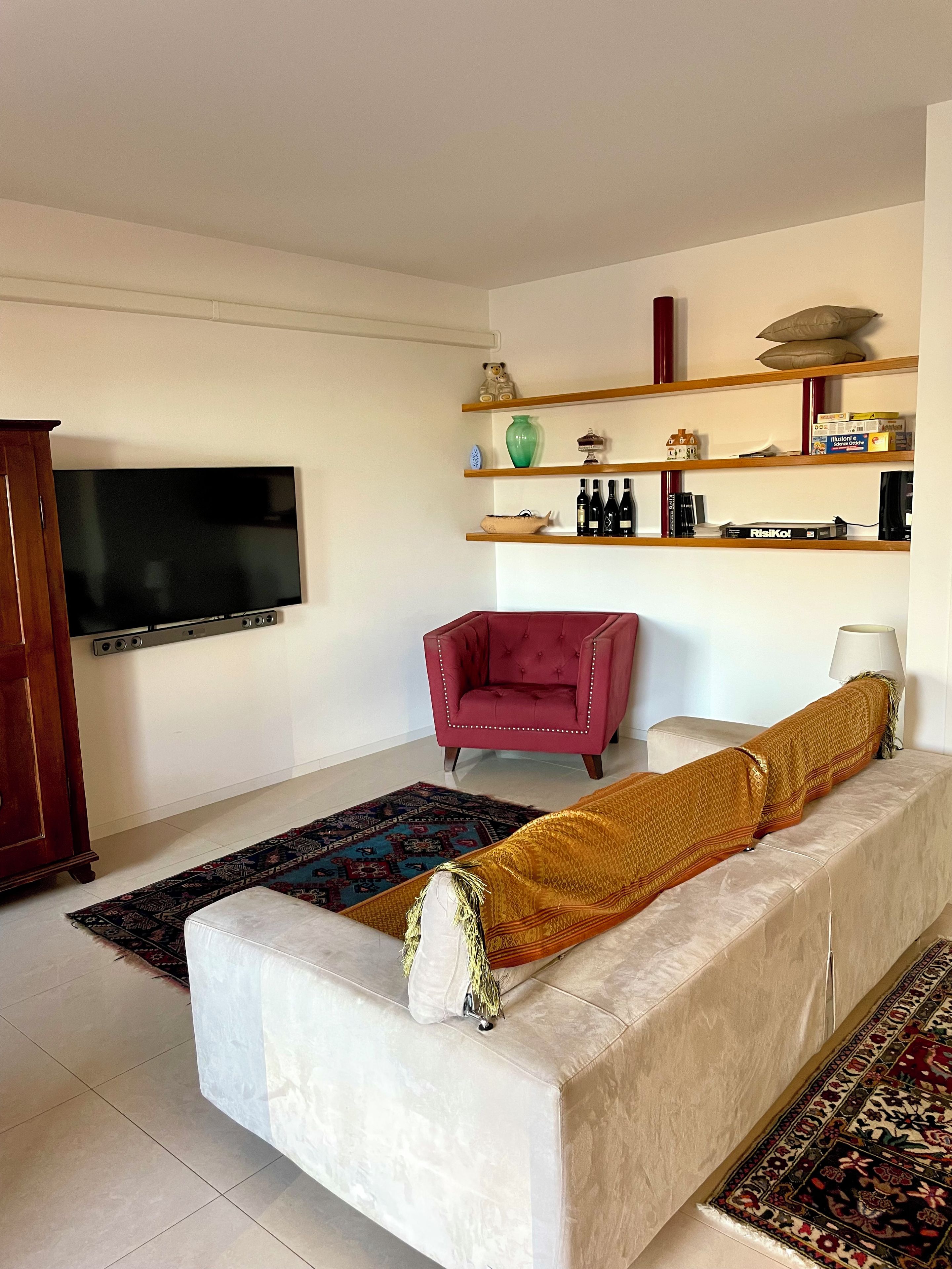 Ein Wohnzimmer mit einem Flachbildfernseher, einem roten Sessel, einem beigen Sofa mit gemustertem Überwurf und einem Couchtisch.