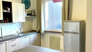 A kitchen with a marble countertop, a refrigerator, a clock, and a window with curtains. - HOLIDAY APARTMENT IN THE HEART OF VALPOLICELLA (San Pietro In Cariano)