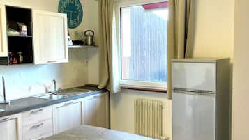 Uma cozinha com bancada de mármore, geladeira, relógio e janela com cortinas.
