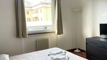 Quarto de hotel com cama, cômoda, radiador e janela com cortinas.