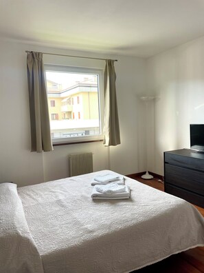 Quarto de hotel com cama, cômoda, radiador e janela com cortinas.