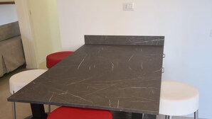 Una mesa de comedor con tapa de mármol oscuro y dos taburetes rojos.