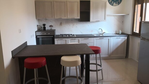 Una cocina moderna con una isla central, taburetes de bar, un reloj y un refrigerador.