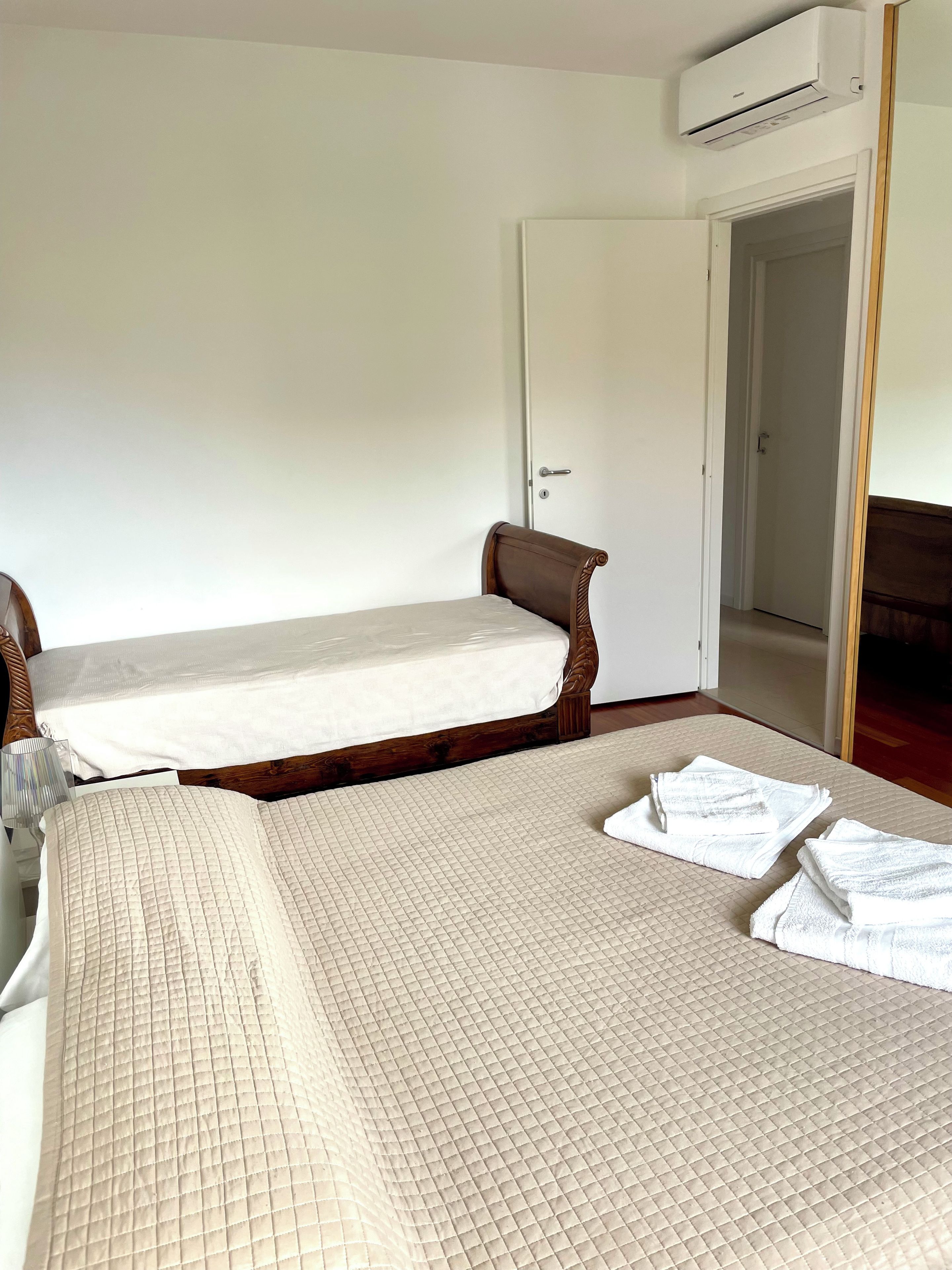 A room with two single beds, a wooden headboard, a white door, and an air conditioning unit.