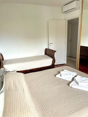 A room with two single beds, a wooden headboard, a white door, and an air conditioning unit. - HOLIDAY APARTMENT IN THE HEART OF VALPOLICELLA (San Pietro In Cariano)