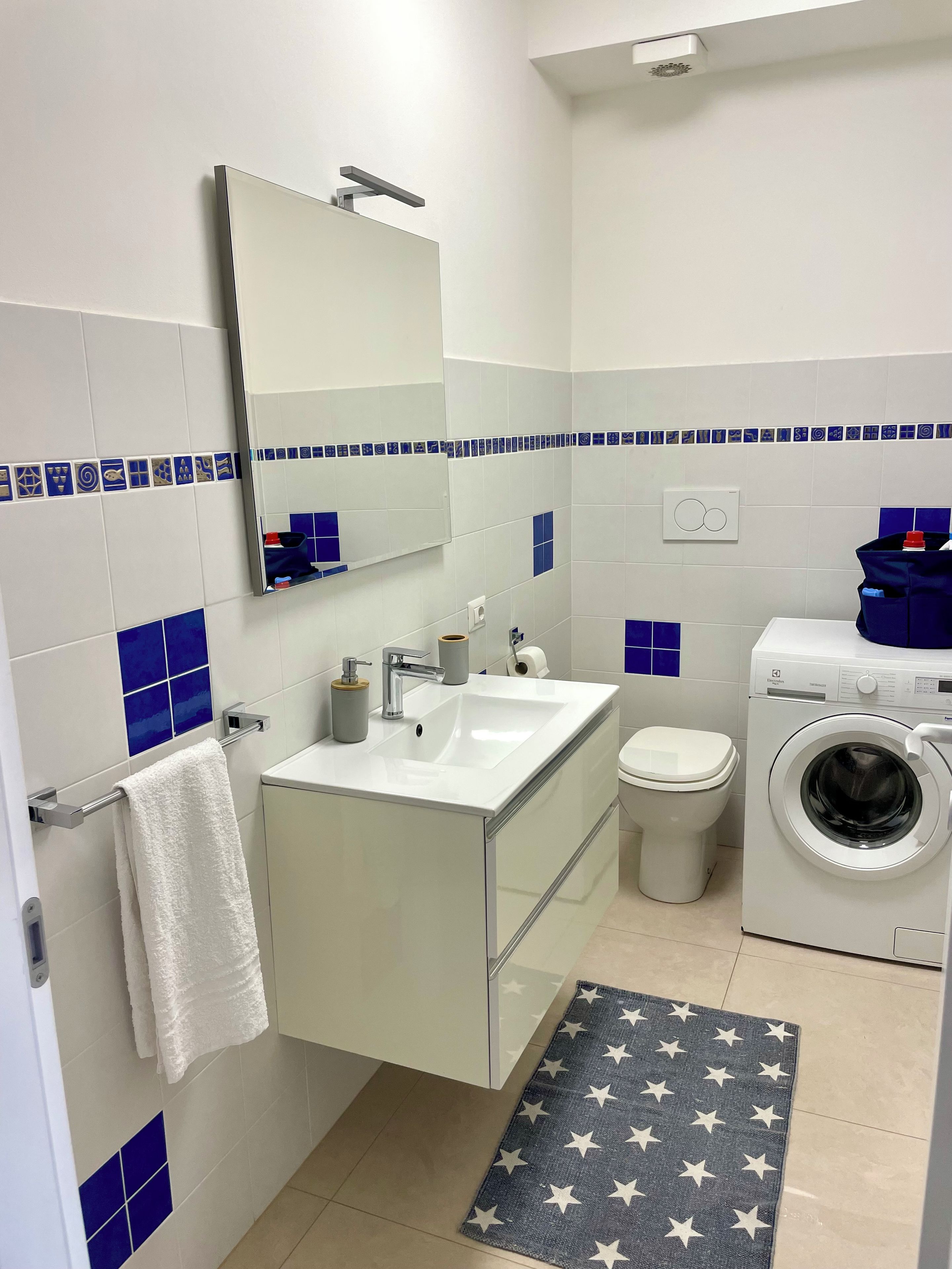 Et badeværelse med vask, spejl, toilet og vaskemaskine.
