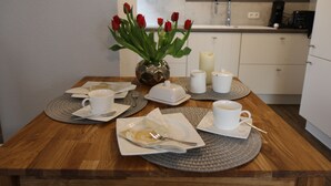 A wooden dining table with a vase of red roses, white cups, saucers, and a plate with a fork. - Apartment "Am See" 2 (Rhauderfehn)