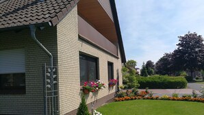 A two-story brick house with a sloped roof, a small front yard with a flower bed, and a well-maintained lawn. - Apartment "Am See" 2 (Rhauderfehn)