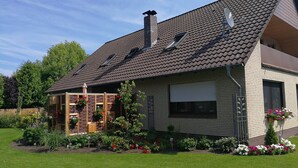 A house with a sloped roof, a brick exterior, and a covered porch with flower boxes. - Apartment "Am See" 2 (Rhauderfehn)