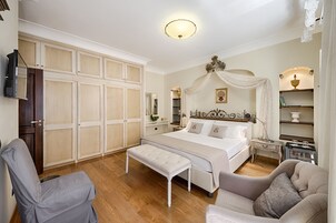 A bedroom with a large bed, a bench, two armchairs, a wardrobe, and a television.