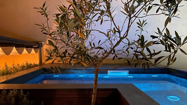 A pool area with a tree in a planter, surrounded by a low wall and a wooden deck. - Relais 147 (Taormina)