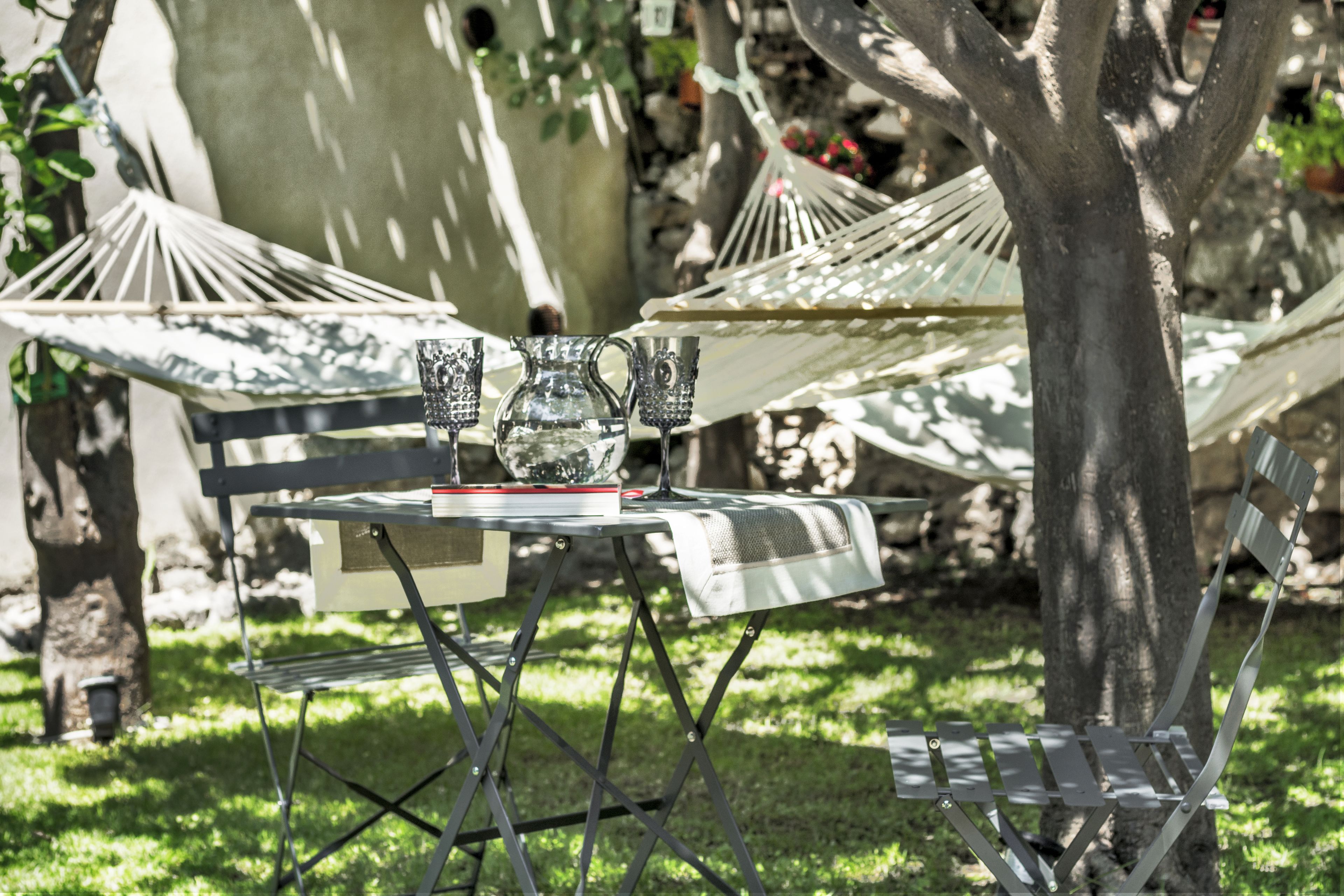 A hammock and a metal table with a glass pitcher and cups.