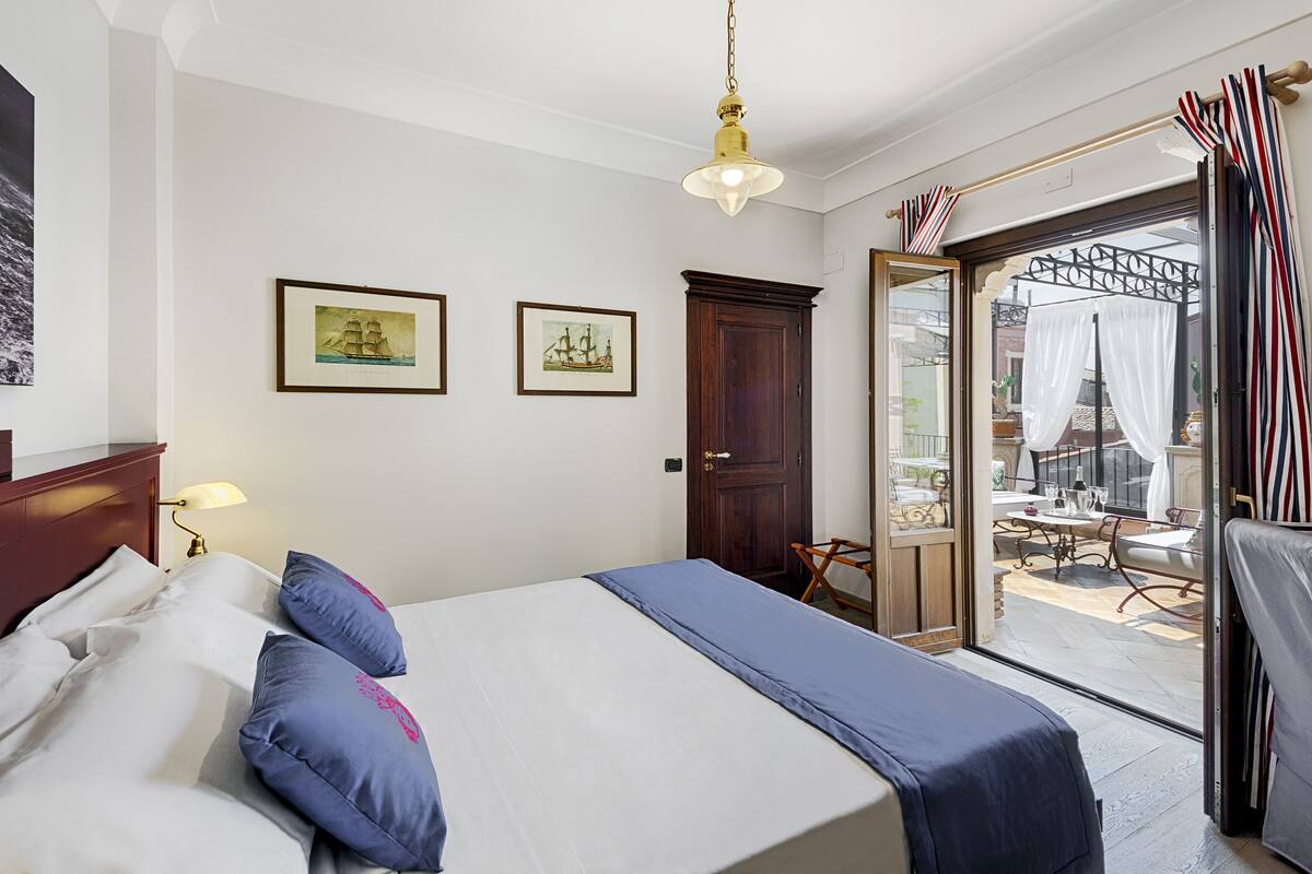 Ein Hotelzimmer mit Bett, Holzschrank, einer Tür und einem Balkon mit Tisch und Stühlen.