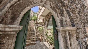 An arched stone doorway leading to a courtyard with a staircase, a large vase, and a door with a keypad. - Relais 147 (Taormina)