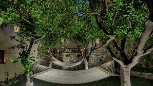 A hammock under a tree with lanterns, a stone wall, and a grassy area. - Relais 147 (Taormina)
