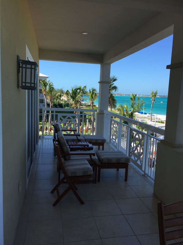 A balcony with a view of the ocean, equipped with wooden chairs and a small table.