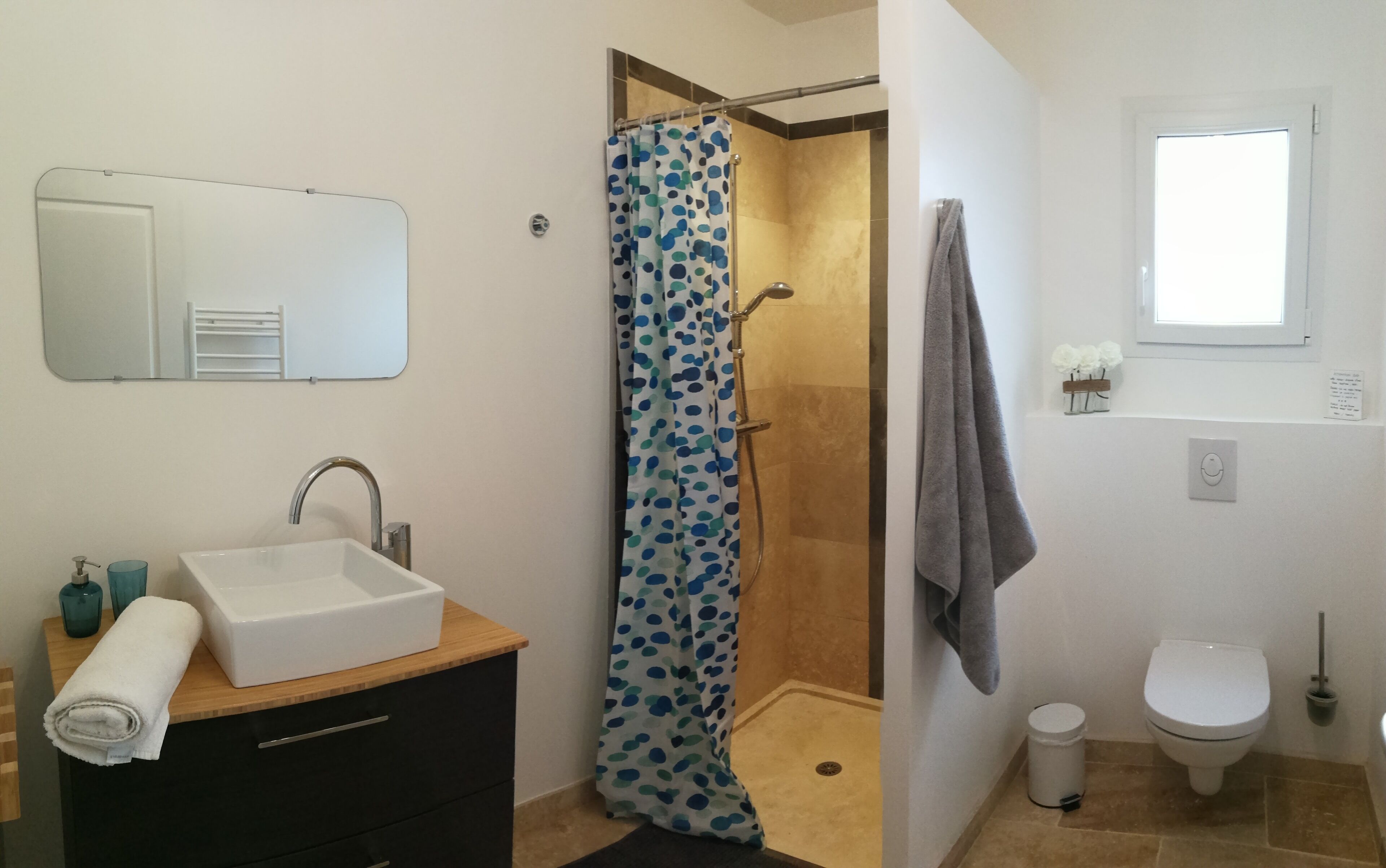 Een badkamer met een witte wastafel, een douche met een stippen gordijn, een toilet en een spiegel boven de wastafel.