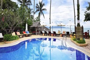 A poolside area with lounge chairs and umbrellas, surrounded by palm trees and a view of the sea. - Lawana Resort Samui (Koh Samui)