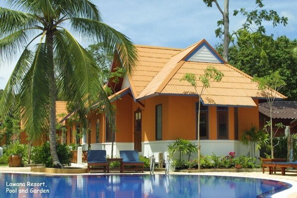 A resort with a swimming pool and garden, featuring a building with a tiled roof and palm trees.