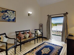 A room with a bench, a rug, a painting, and a view of a body of water. - Mercure Goa Devaaya Resort (Panaji)