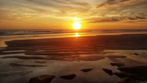 Atardecer sobre una playa con mar tranquilo y rocas dispersas.