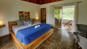 Un dormitorio con una cama de madera, una colcha azul, un cuadro en la pared y vistas al exterior a través de una puerta corredera.