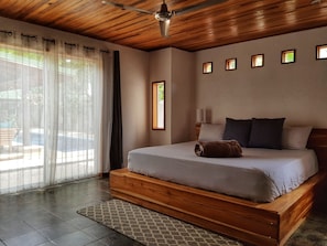 Une chambre à coucher avec un lit en bois, une vue sur l’extérieur par une fenêtre et un ventilateur de plafond.