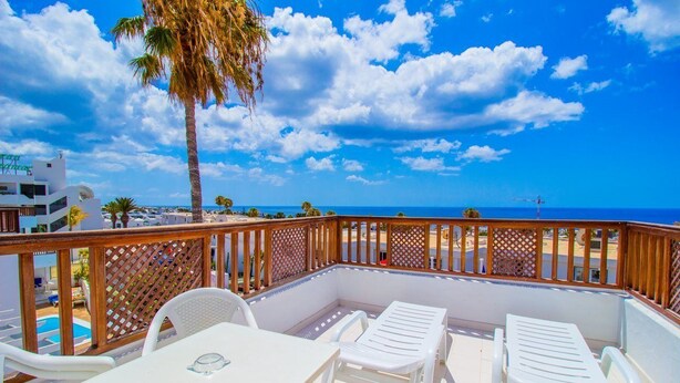 A balcony with white furniture, a pool, and a view of the beach and ocean. - Vista Mar Apartamentos (Tías)