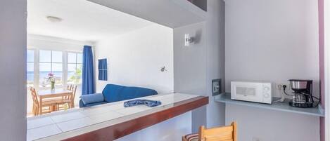 A compact kitchen with a microwave, coffee maker, and a dining area with a blue sofa and wooden chairs.