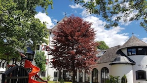 Un'area giochi con uno scivolo rosso, immersa nel verde e con un grande albero dai fogliame rossi.