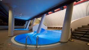 Piscina interna con elemento d'acqua blu, circondata da colonne bianche e un soffitto curvo.