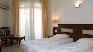 A hotel room with two beds, a desk, chairs, a window with curtains, and a wall-mounted lamp. - Alin Hotel (Alanya)