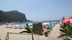 A beach with sun loungers, umbrellas, and a wooden structure. - Alin Hotel (Alanya)