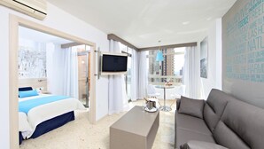 A modern hotel room with a bed, a sofa, a TV, a small table, and a cityscape view. - Flamingo Beach Resort (Benidorm)