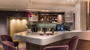 Un espace bar moderne avec un comptoir en marbre, des chaises violettes et une variété de bouteilles et de verres.