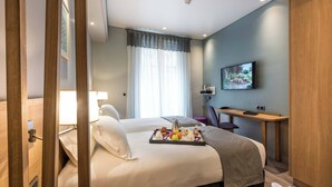Une chambre d’hôtel avec un lit, un bureau, une télévision et un plateau de petit-déjeuner.