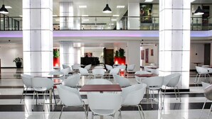 A spacious indoor area with multiple white tables and chairs, a central counter, and a staircase leading to an upper level. - Radisson Hotel Paramaribo (Paramaribo)