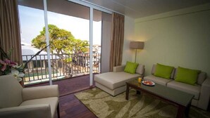 A modern living room with a sofa, armchair, and coffee table. There is a balcony with a view of trees and buildings. - Radisson Hotel Paramaribo (Paramaribo)