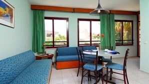 A room with a blue sofa, a dining table with chairs, and large windows with green curtains. - Caprice Apartments (Alanya)