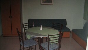 A small dining area with a round table, four chairs, a green tablecloth, a white vase, and a framed picture on the wall. - Caprice Apartments (Alanya)