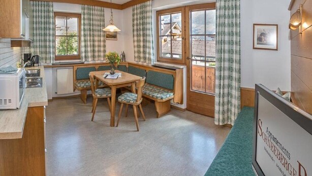 A cozy kitchen with a dining area, featuring a wooden table and chairs, a radiator, and a view of the outside. - Guesthouse Schneeberger (Zell am Ziller)