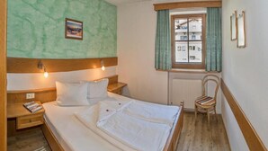 A bedroom with a bed, bedside tables, a chair, a window with curtains, and a wall-mounted picture. - Guesthouse Schneeberger (Zell am Ziller)