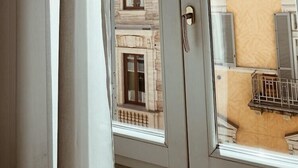 A view through a window with a white frame and a door, revealing a building with multiple windows and balconies. - Residenza Sciarra (Rome)