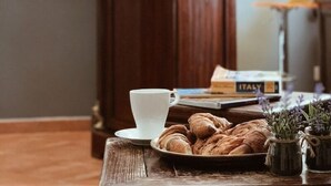 A table with a white cup, a plate of croissants, and a book titled "ITALY" in a room with a wooden cabinet and a painting of a cityscape. - Residenza Sciarra (Rome)