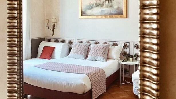 A bedroom with a large bed, a small bedside table, a painting on the wall, and a decorative ceiling. - Residenza Sciarra (Rome)