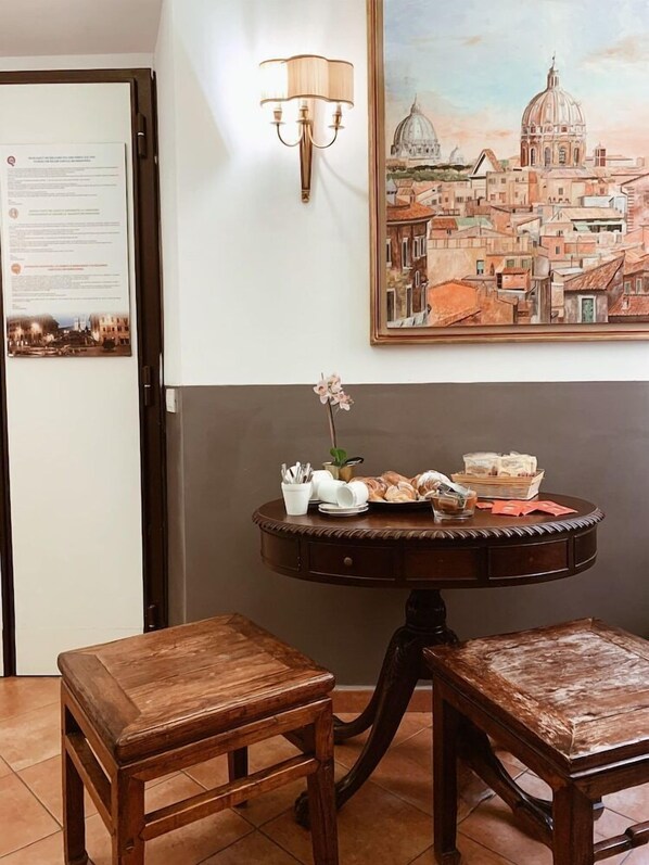 A room with a dining table set with plates, a vase with flowers, and a lamp. There is a painting of a cityscape on the wall. - Residenza Sciarra (Rome)